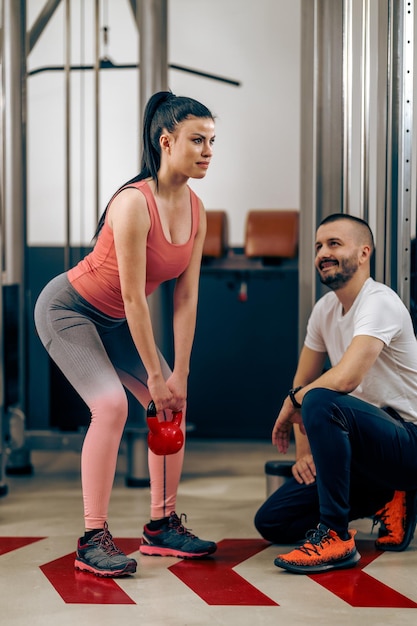 Jeune femme fait des exercices avec kettlebell pendant l'entraînement avec un entraîneur personnel dans la salle de gym.