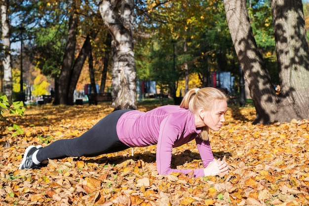 Jeune femme fait des exercices de planche dans le parc Sports à l'extérieur en automne