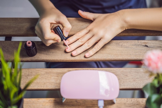 Une jeune femme fait une manucure avec du vernis gel et une lampe UV dans les tons roses