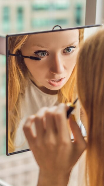 La jeune femme fait le maquillage s'asseyant par la fenêtre avec une vue panoramique des gratte-ciel et du grand