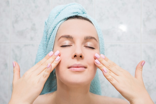 Jeune femme fait un massage du visage avec les mains dans la salle de bain.