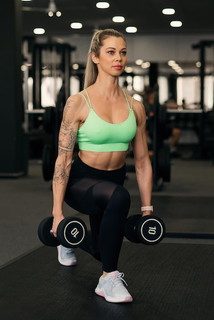 Une jeune femme fait des sauts avec des haltères au gymnase.