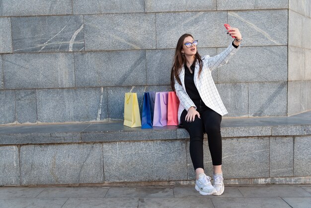 Jeune femme fait selfie avec des sacs colorés. Blogger de mode. Après les achats.