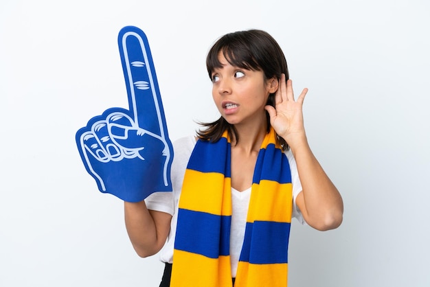 Jeune femme de fan de sport de race mixte isolée sur fond blanc écoutant quelque chose en mettant la main sur l'oreille