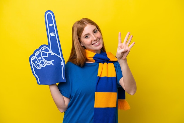 Jeune femme fan de sport rousse isolée sur fond jaune heureuse et comptant quatre avec les doigts