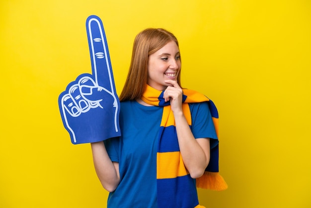 Jeune femme fan de sport rousse isolée sur fond jaune regardant sur le côté et souriant