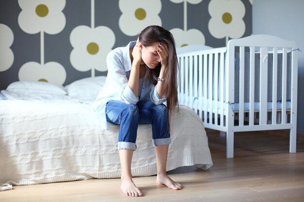 Jeune femme fatiguée assise sur le lit près du lit d'enfant