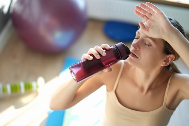 Une jeune femme fatiguée boit de l'eau après une formation en gros plan