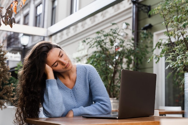 Une jeune femme fatiguée fait une pause au travail et dort et se détend sur un ordinateur portable sur le lieu de travail en raison des heures supplémentaires Fille endormie avec un ordinateur portable sur la table en plein air dans un café