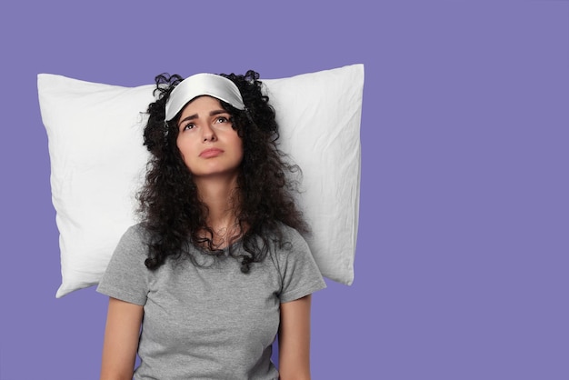 Photo jeune femme fatiguée avec masque de sommeil et oreiller sur fond violet espace pour le texte problème d'insomnie