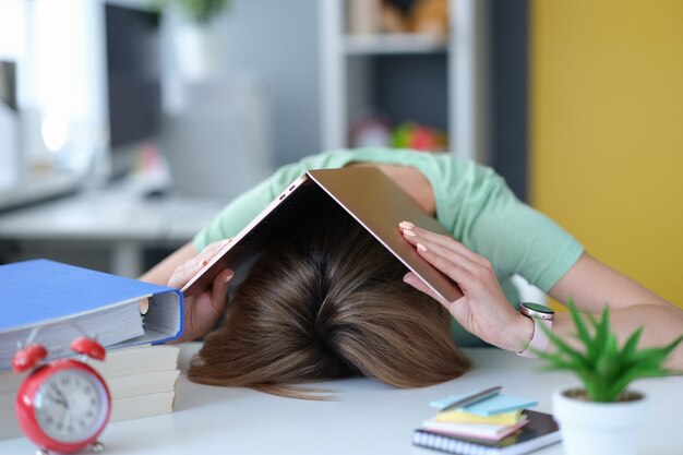 Une jeune femme fatiguée se trouve sur la table sur la tête avec un ordinateur portable