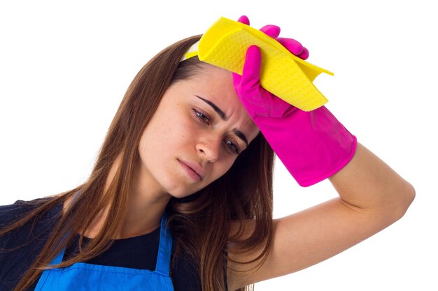 Jeune femme fatiguée en T-shirt bleu et tablier avec des gants roses tenant un chiffon et un détergent en studio