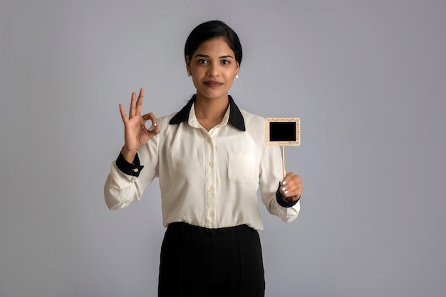 Jeune femme ou femme d'affaires tenant une petite planche à découper dans ses mains sur un mur gris.