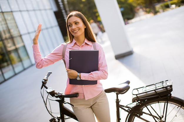 Jeune femme avec des fichiers dans les mains, debout en plein air à côté de vélo électrique
