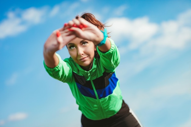 Photo jeune femme de fitness faisant des exercices d'étirement après avoir fait du jogging dans la nature. derrière c'est un ciel clair avec des nuages.