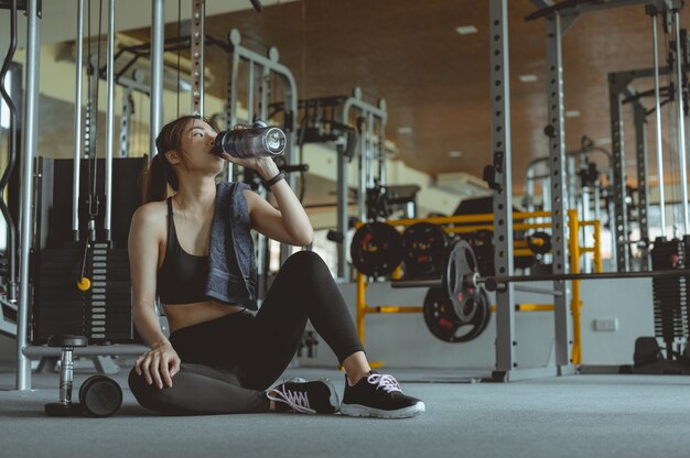 Jeune femme fitness fatiguée dans la salle de gym boire de l'eau Fitness entraînement gym exercice mode de vie et sain