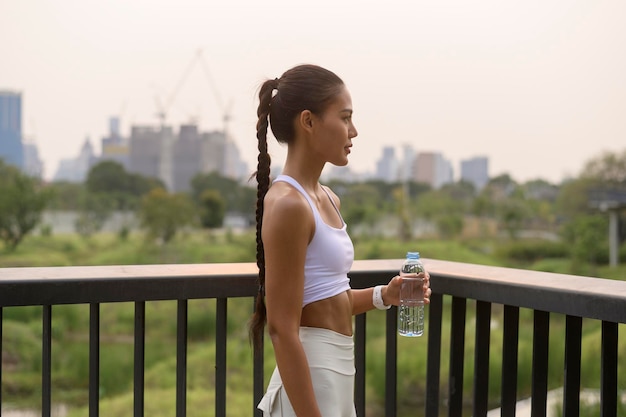 Jeune femme de fitness en tenue de sport buvant de l'eau dans le parc de la ville