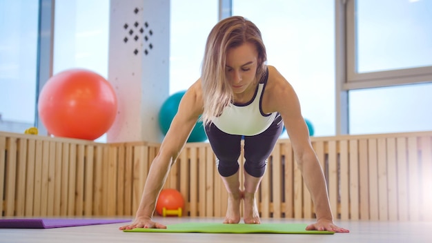 Jeune femme fitness trainer faisant des pompes dans le studio lumineux