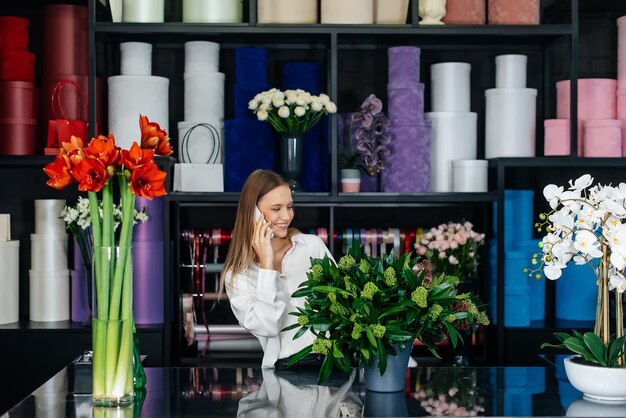 Une jeune femme fleuriste accepte une commande par téléphone pour la réalisation d'un beau bouquet festif