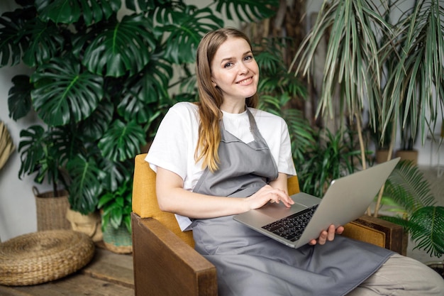 Une jeune femme fleuriste employé fleur atelier plantes pour la maison à l'aide d'un ordinateur portable assis