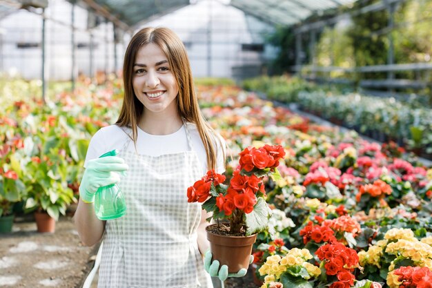 Jeune femme fleuriste pulvérisant de l'eau sur les plantes d'intérieur dans des pots de fleurs par pulvérisateur