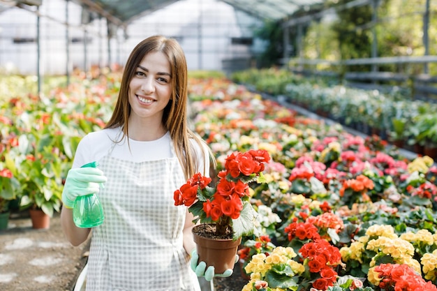 Jeune femme fleuriste pulvérisant de l'eau sur les plantes d'intérieur dans des pots de fleurs par pulvérisateur