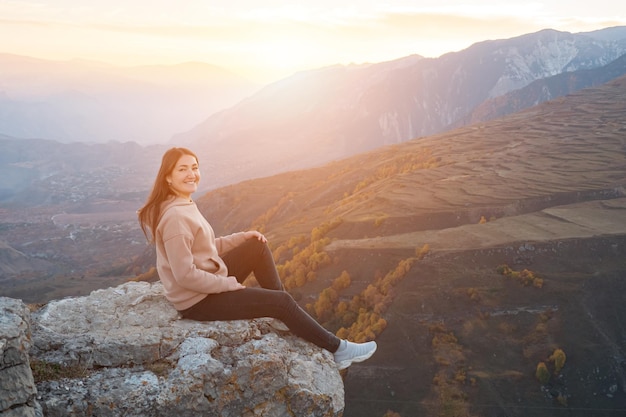 Jeune femme sur fond d'arbres jaunes est assise sur un rocher saillant, la lumière du soleil.