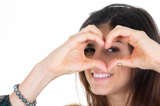 Jeune femme sur fond blanc souriant et montrant une forme de coeur avec les mains sur le visage