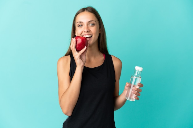 Jeune femme sur fond bleu isolé avec une bouteille d'eau et manger une pomme