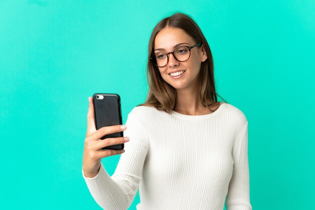 Jeune femme sur fond bleu isolé faisant un selfie avec téléphone mobile