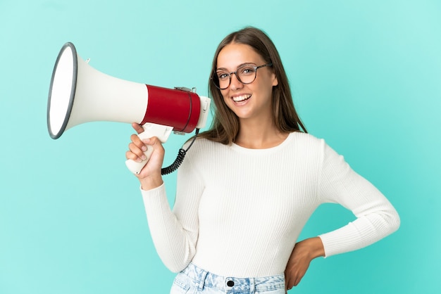 Jeune femme sur fond bleu isolé tenant un mégaphone et souriant