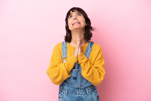 Jeune femme avec fond isolé salopette maintient la paume ensemble. La personne demande quelque chose