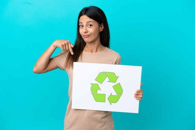 Jeune femme sur fond isolé tenant une pancarte avec l'icône de recyclage et le pointant