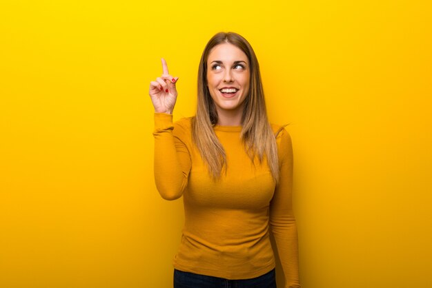 Jeune femme sur fond jaune ayant l’intention de réaliser la solution tout en levant le doigt