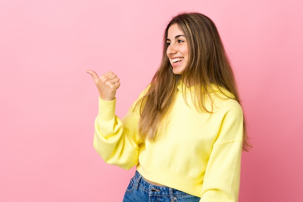 Jeune femme sur fond rose isolé pointant vers le côté pour présenter un produit