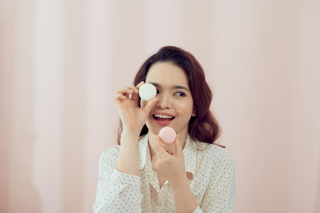 Jeune femme sur fond rose isolé tenant des macarons français colorés avec une grimace