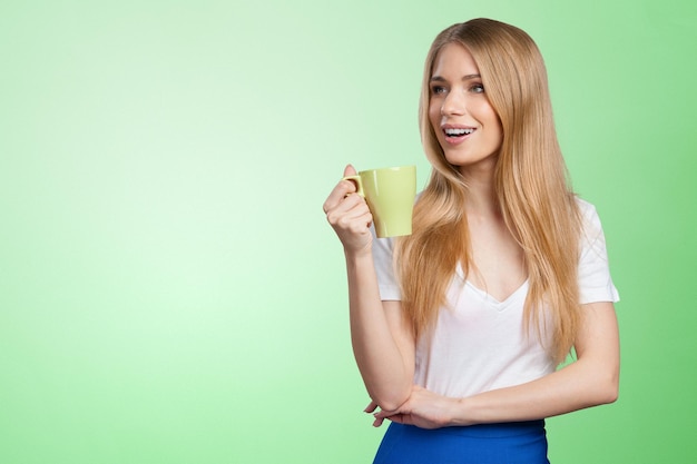 Jeune femme sur fond de studio boit du café ou du thé