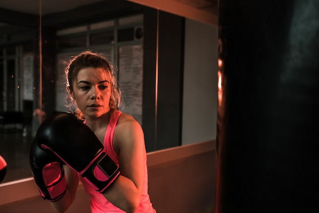 Jeune femme en formation avec un sac de boxe lourd dans la salle de gym. Moment avant le coup de poing.