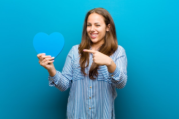 Jeune femme en forme de coeur contre le bleu