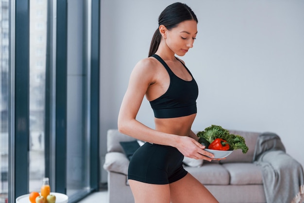 Jeune femme avec une forme de corps mince en vêtements de sport noirs a une journée de remise en forme à l'intérieur à la maison