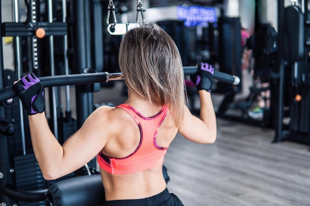 Jeune femme en forme faisant des exercices d'épaules à l'aide d'une machine d'entraînement dans une salle de sport. Vue de dos.