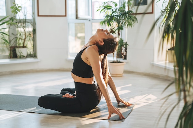 Jeune femme en forme pratique le yoga faisant des asanas dans un studio de yoga léger avec une plante verte