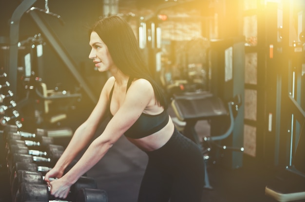 Jeune femme en forme de prendre un haltère du rack dans la salle de gym.