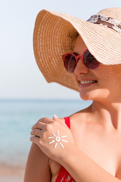 Jeune femme avec une forme de soleil sur sa main faite de crème solaire à la plage.