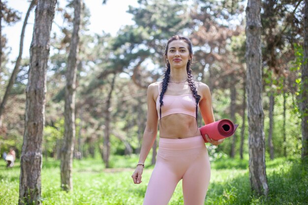 Jeune femme en forme avec un tapis de yoga dans la forêt