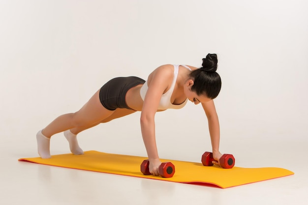 Jeune femme forte faisant des exercices de pompes avec des haltères.