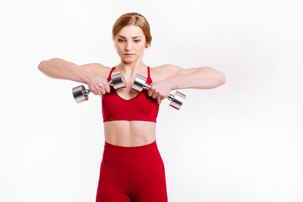 Jeune femme forte et sportive en tissu rouge faisant des exercices avec des haltères sur fond blanc