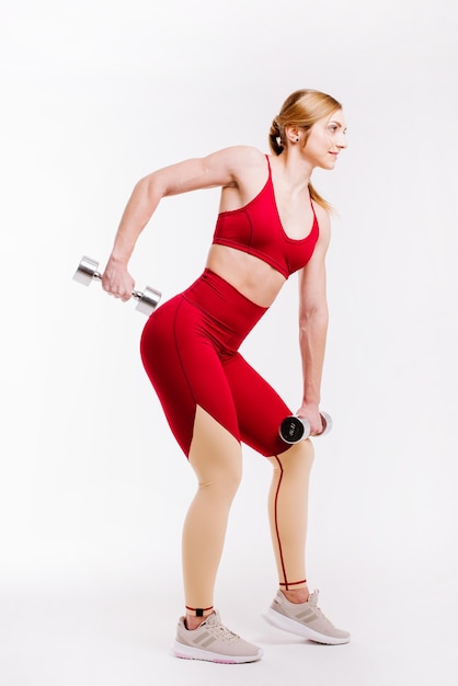 Jeune femme forte et sportive en tissu rouge faisant des exercices avec des haltères sur fond blanc