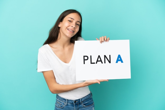 Jeune femme française isolée sur fond bleu tenant une pancarte avec le message PLAN A avec expression heureuse