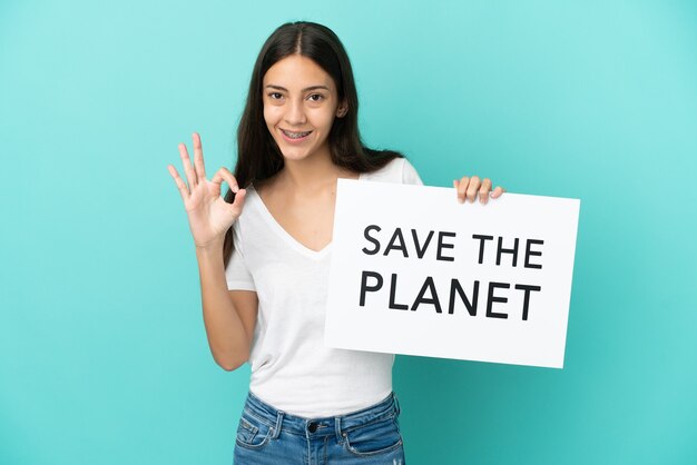 Jeune femme française isolée sur fond bleu tenant une pancarte avec texte Save the Planet et célébrant une victoire